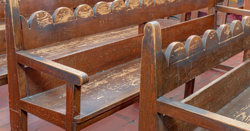 A row of well-worn church pews made of wood is in need of refinishing. They’ve got a lot of scratches.