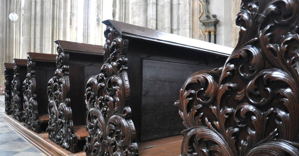 A row of fancy church pews with intricate carvings on them in a church with marble walls and a tiled floor.